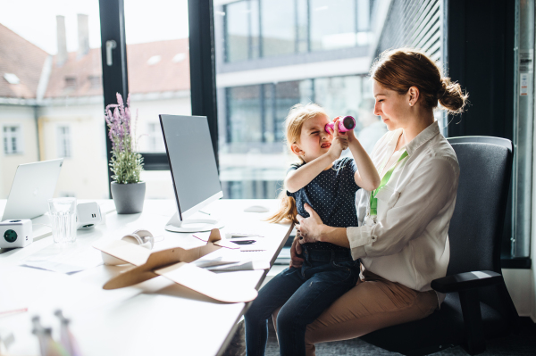 A businesswoman with a small daughter sitting in an office, working.