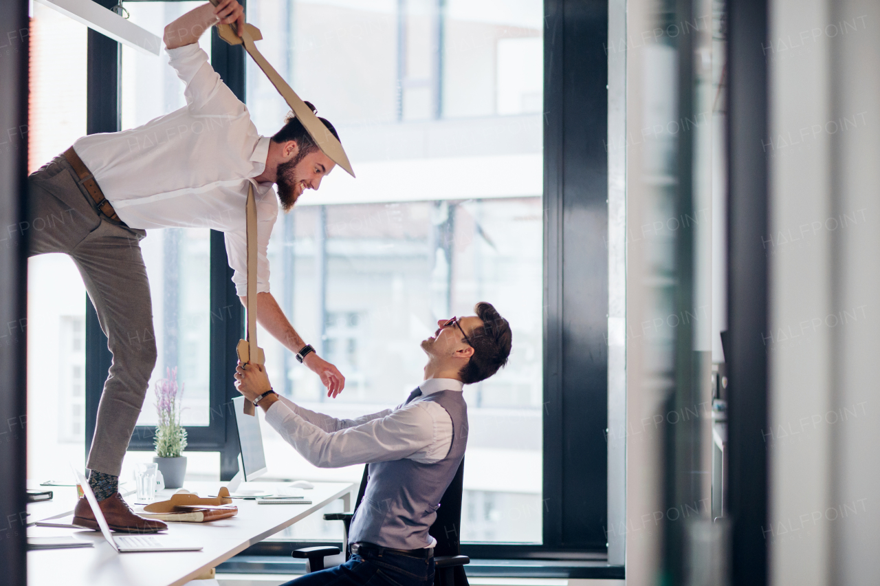 Two young businessmen with cardboard swords in an office, having fun. A competition concept.