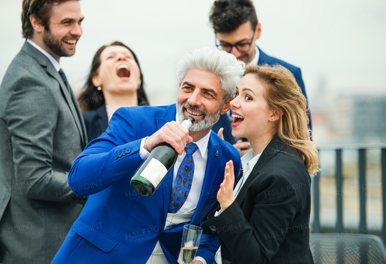 A large group of joyful businesspeople having a party outdoors on roof terrace in city.