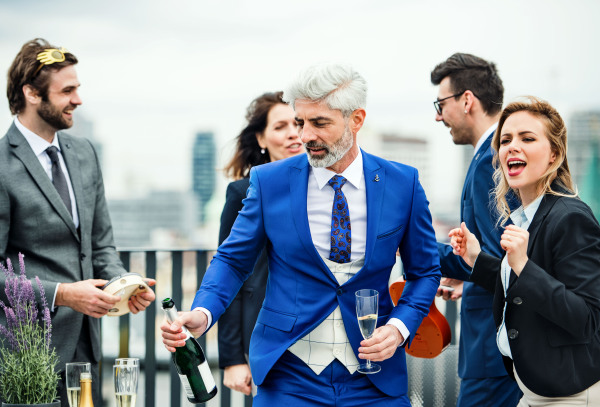 A large group of joyful businesspeople having a party outdoors on roof terrace in city.