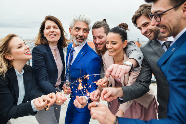 A large group of joyful businesspeople with sparklers having a party outdoors on roof terrace in city.