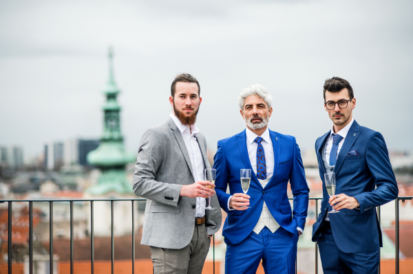 A group of businessmen with champagne standing outdoors on roof terrace in city.