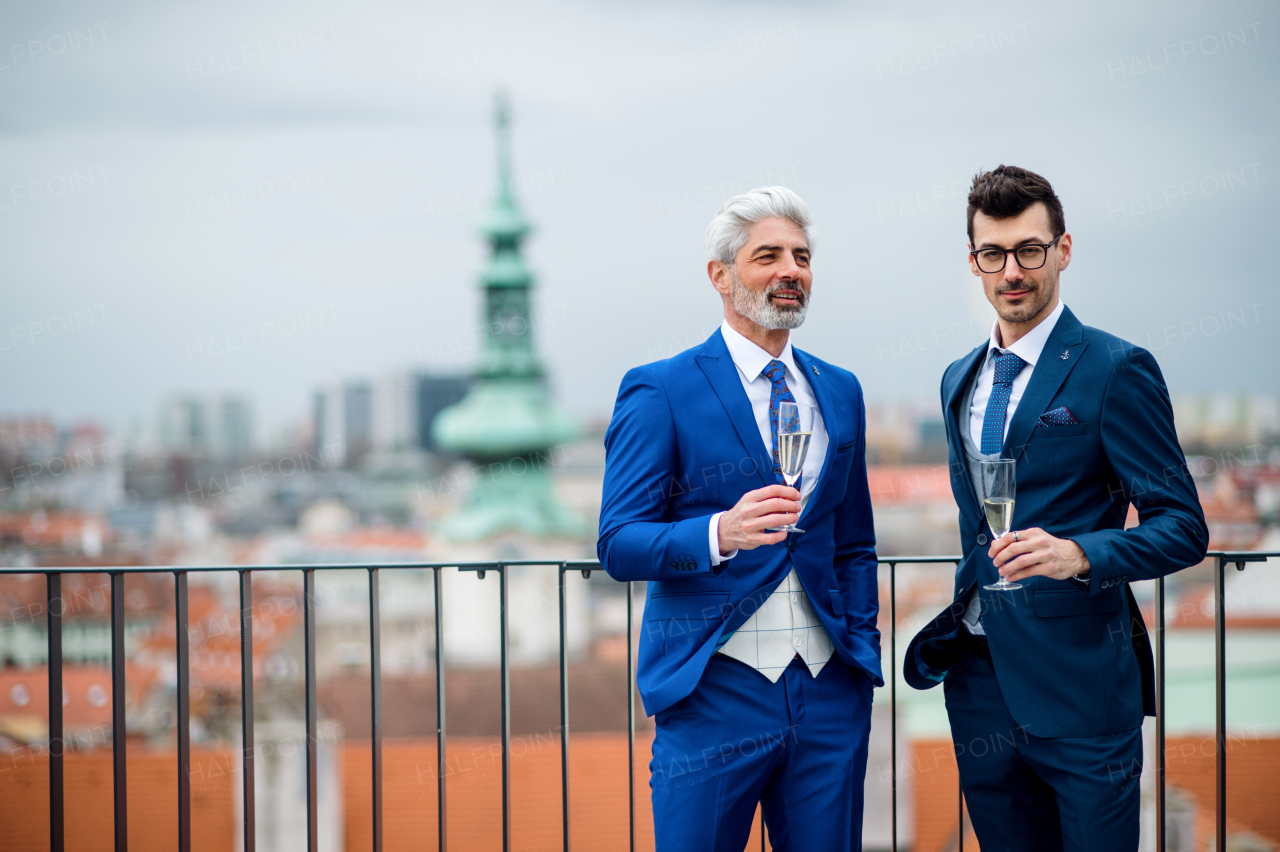 Two businessmen with champagne standing outdoors on roof terrace in city.