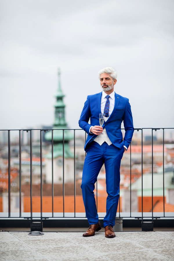 A mature businessman with champagne in glass having a party outdoors on roof terrace in city.