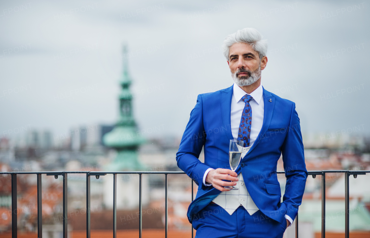 A mature businessman with champagne in glass having a party outdoors on roof terrace in city.