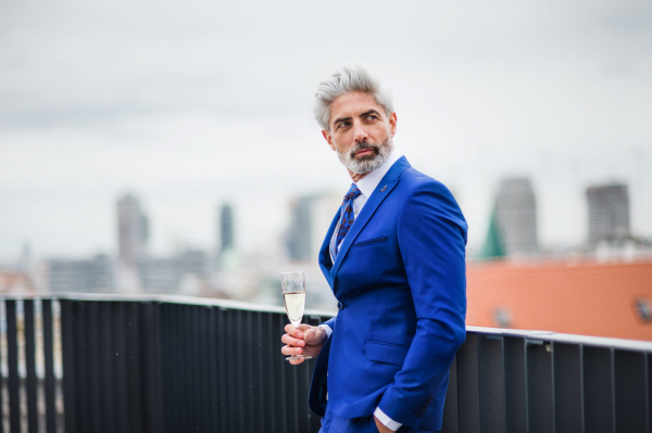 A mature businessman with champagne in glass having a party outdoors on roof terrace in city.