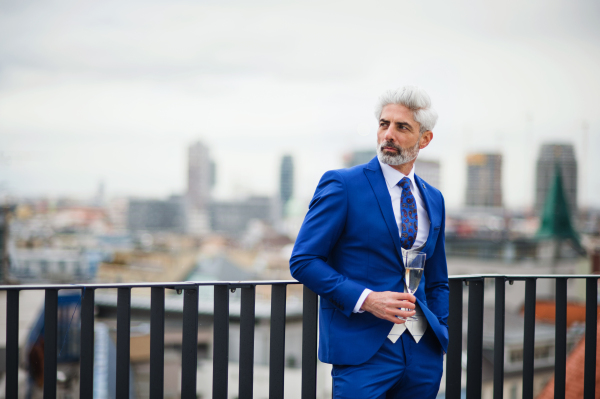 A mature businessman with champagne in glass having a party outdoors on roof terrace in city.