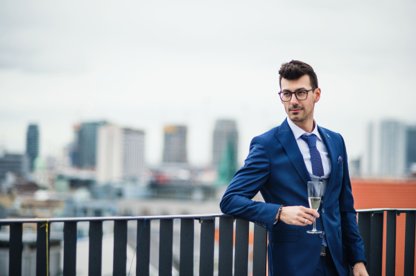 A young businessman with champagne in glass on a party outdoors on roof terrace in city.