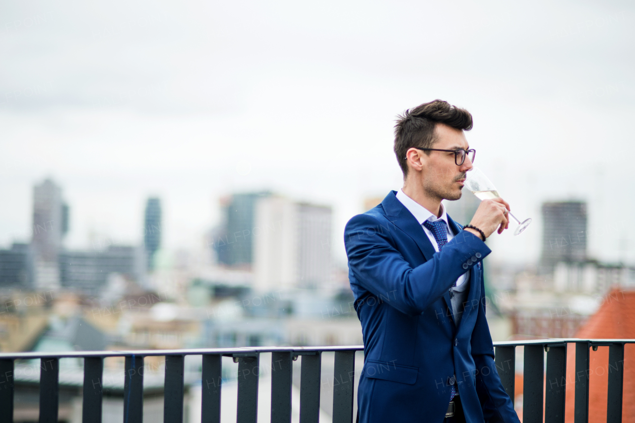 A young businessman with champagne in glass on a party outdoors on roof terrace in city.