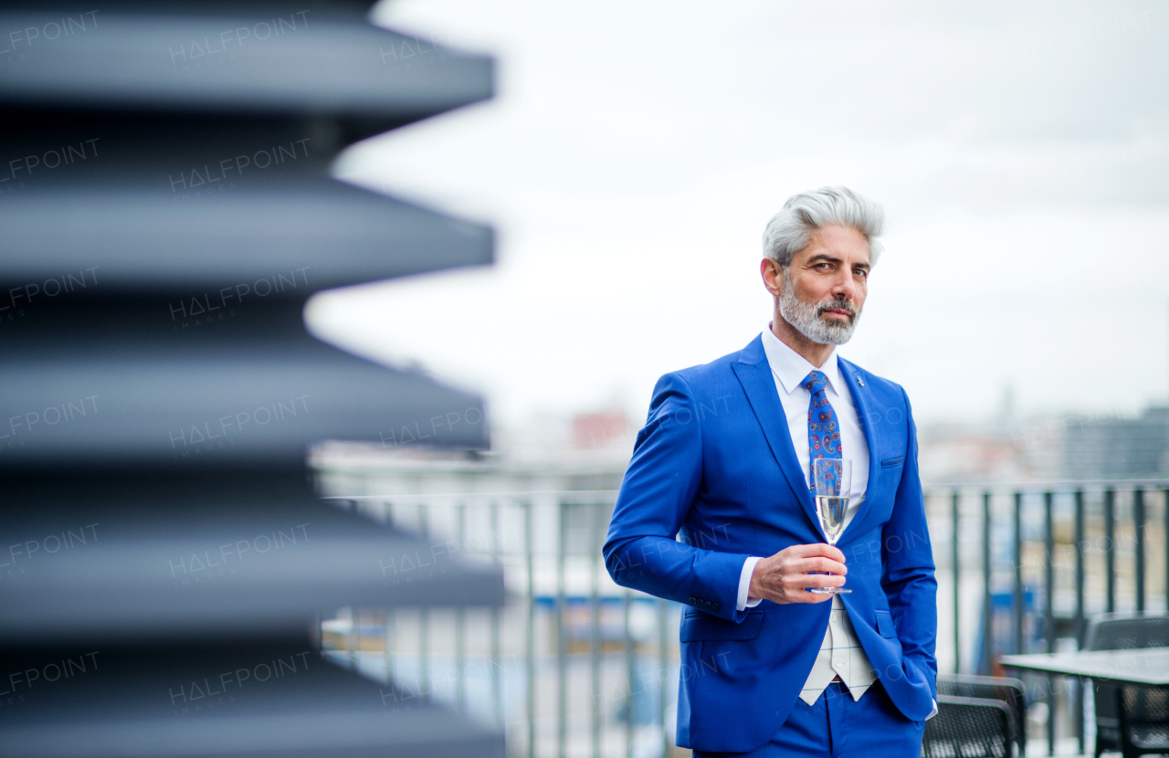 A mature businessman with champagne in glass having a party outdoors on roof terrace in city.