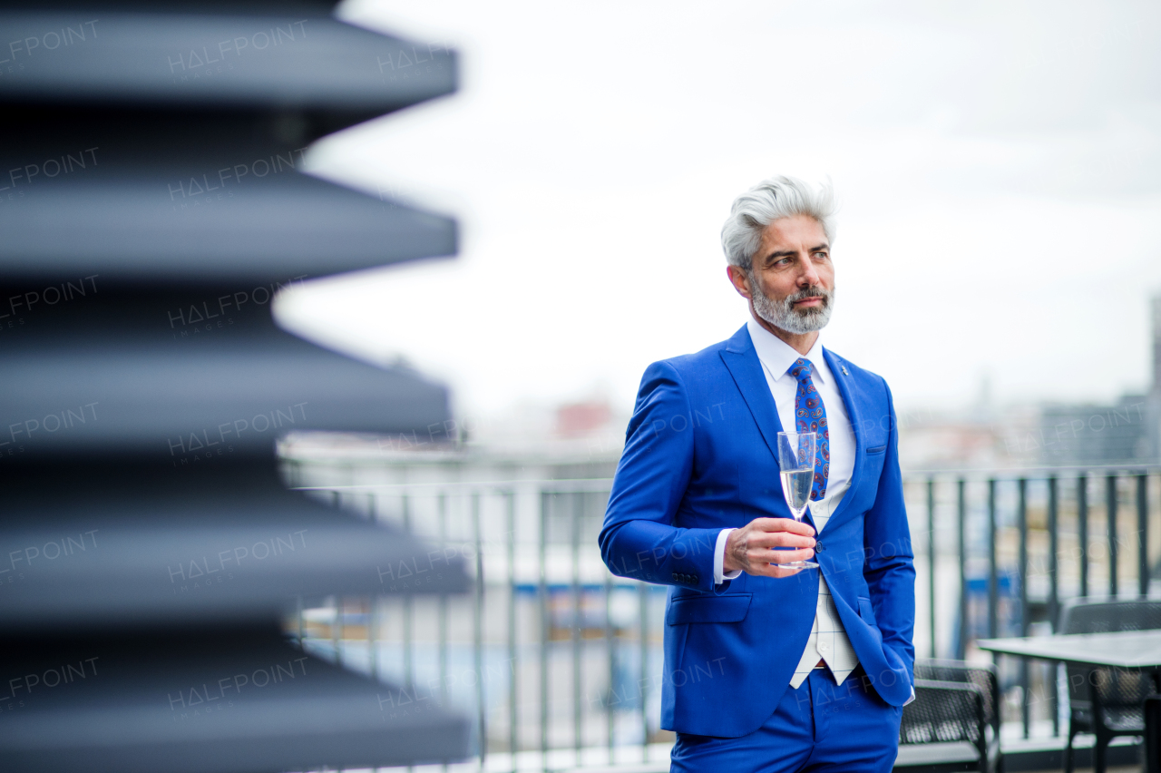 A mature businessman with champagne in glass having a party outdoors on roof terrace in city.