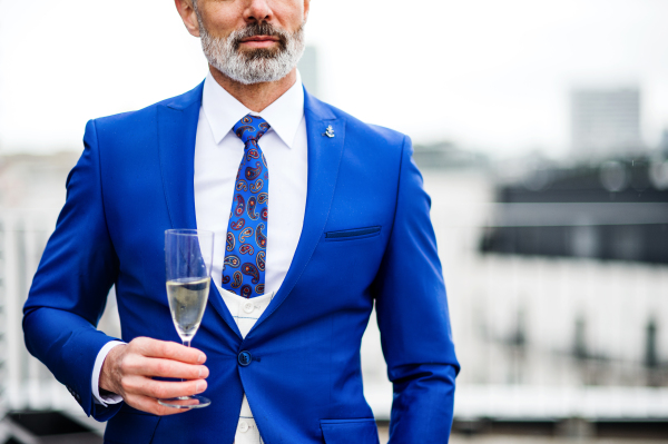 A midsection of mature businessman with champagne in glass having a party outdoors on roof terrace in city.