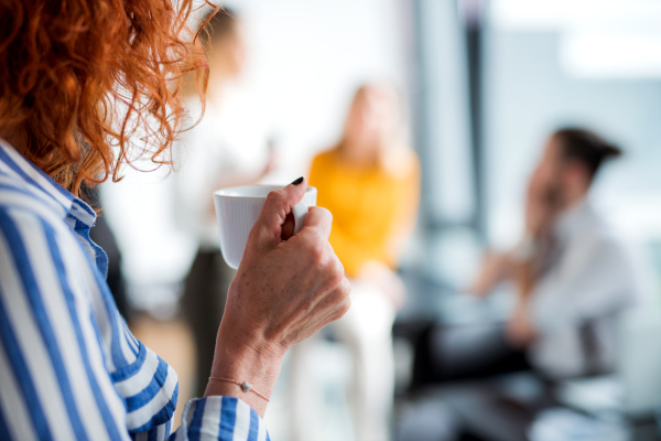 A midsection of unrecognizable businesswoman in an office, holding a cup of coffee.