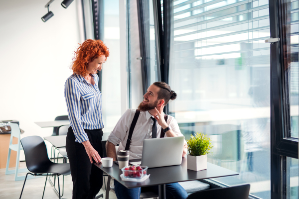 Two cheerful businesspeople in an office, using laptop.