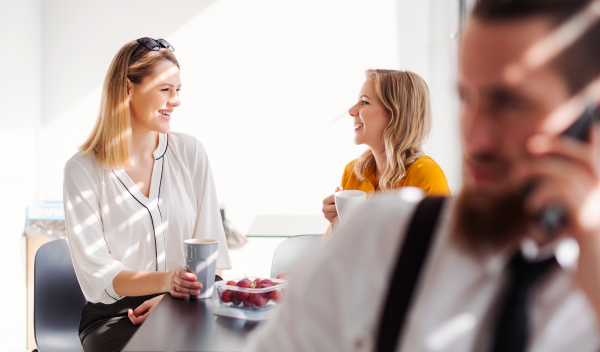 Young cheerful businesswomen on coffee break in office kitchen, talking.