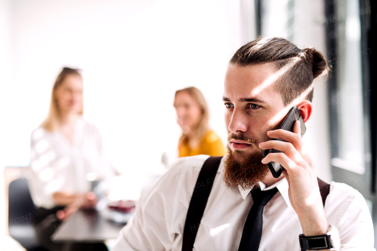 A portrait of young businessman with smartphone in an office, making a phone call.