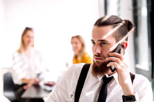 A portrait of young businessman with smartphone in an office, making a phone call.