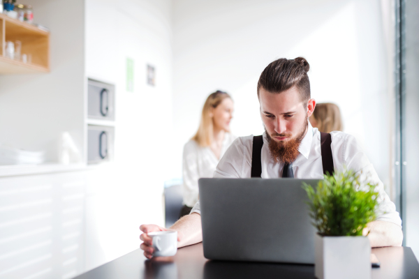 A portrait of happy young businessman with computer in an office, working.