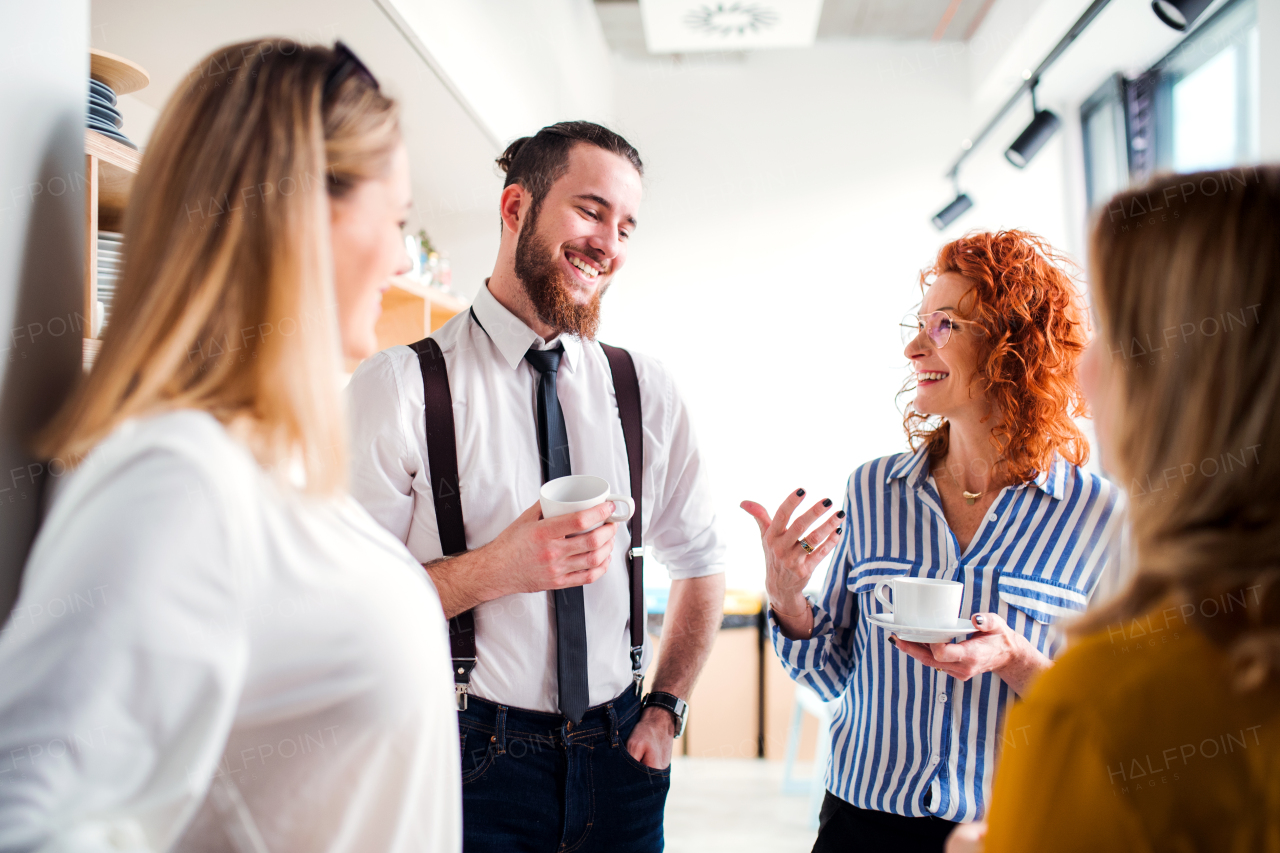 A group of young business people on coffee break in office kitchen, talking.