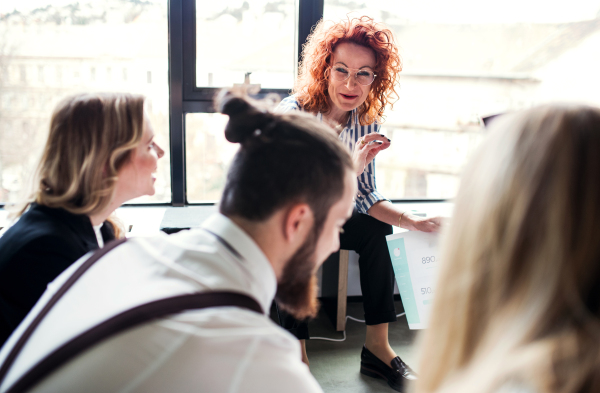 A group of young business people with a diary sitting on the floor in an office, talking.