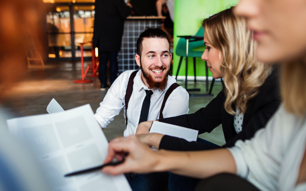 A group of young business people with a diary sitting on the floor in an office, talking.