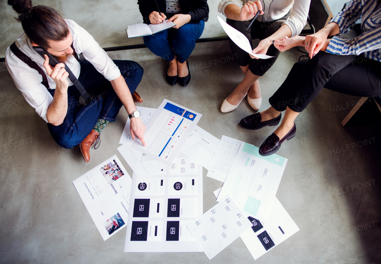 A midsection of group of young business people sitting on the floor in an office. Top view.