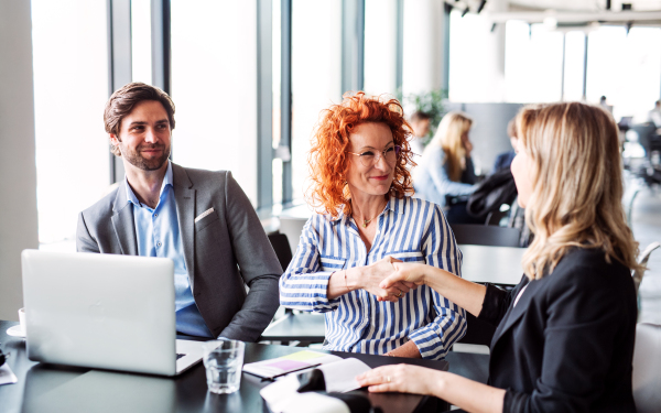 A group of young business people sitting and talking in an office, shaking hands.