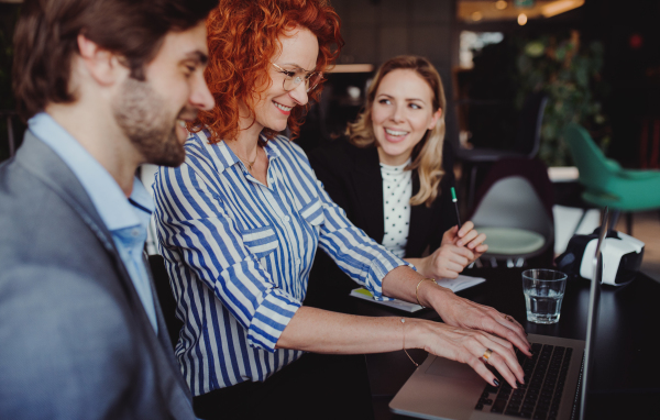 A group of young cheerful business people with laptop sitting in an office, talking.