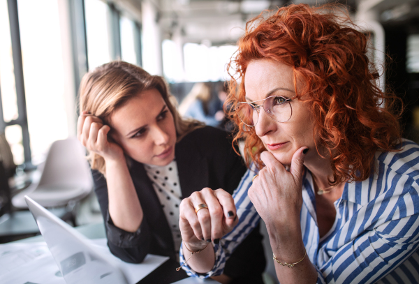 Two serious female business people sitting in an office, talking.