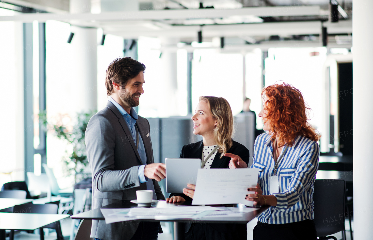 A group of young cheerful business people with tablet sitting in an office, talking.