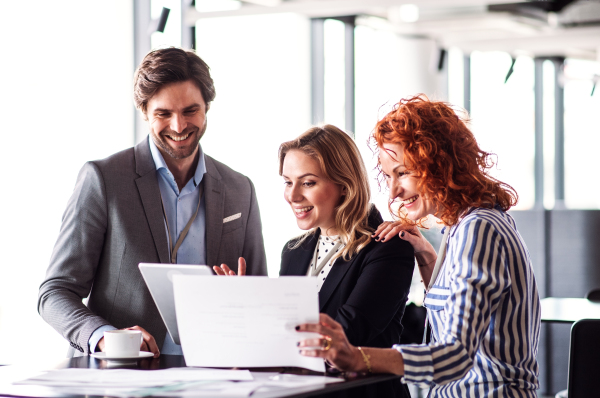 A group of young cheerful business people with tablet sitting in an office, talking.