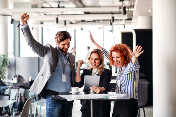 A group of cheerful business people with documents standing in an office, expressing excitement.