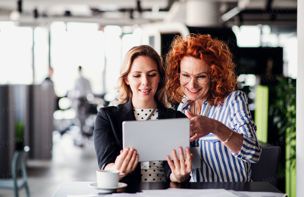 Two serious female business people with tablet sitting in an office, talking.