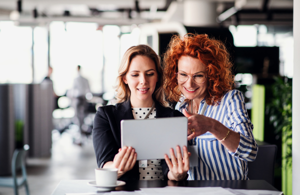 Two serious female business people with tablet sitting in an office, talking.