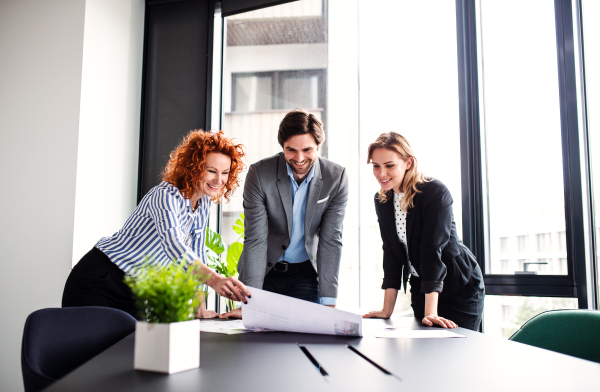 A group of young cheerful business people with documents standing in an office, talking.