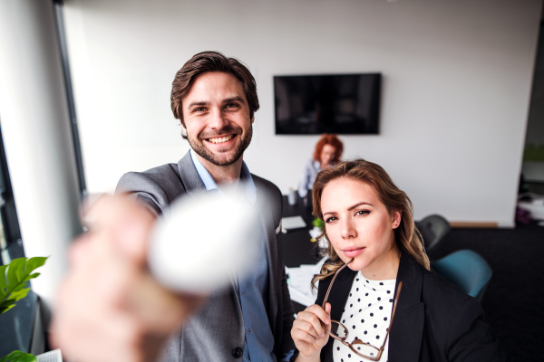 Two young business people standing in an office, looking at camera.