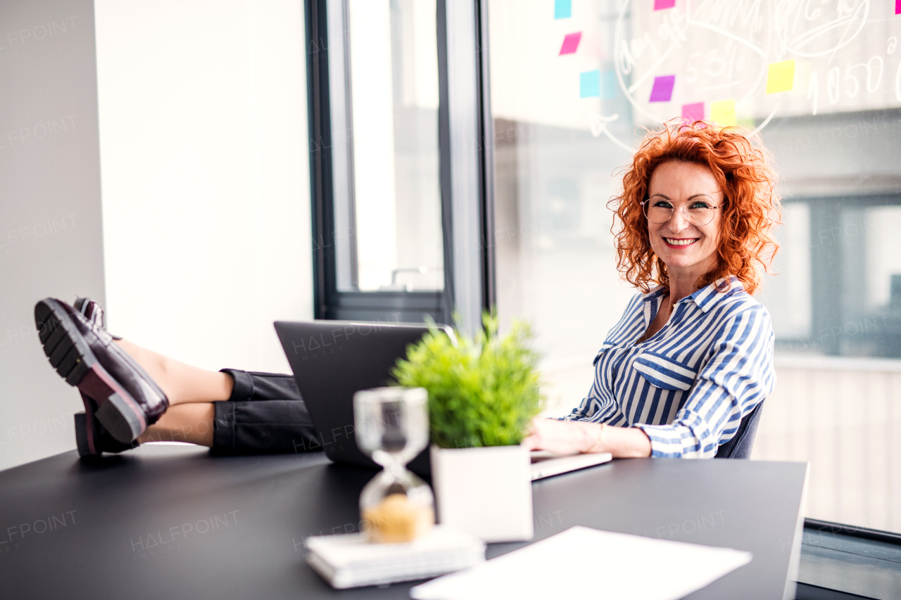 A portrait of businesswoman resting in an office, holding a cup of coffee. Feet on desk.