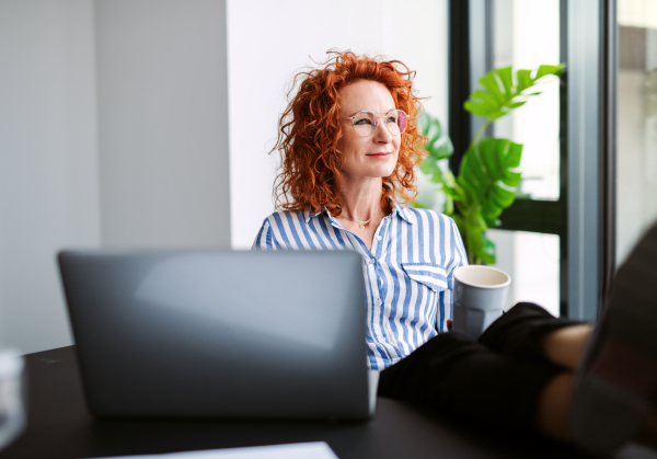 A portrait of businesswoman resting in an office, holding a cup of coffee. Feet on desk.