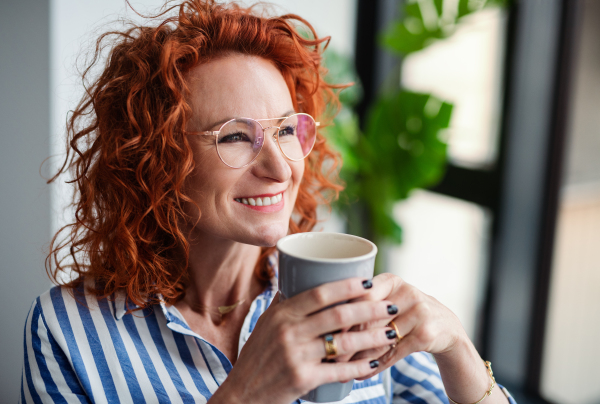 A portrait of happy businesswoman in an office, holding a cup of coffee.