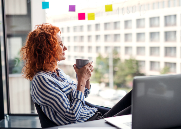 A portrait of mature businesswoman resting in an office, holding a cup of coffee.