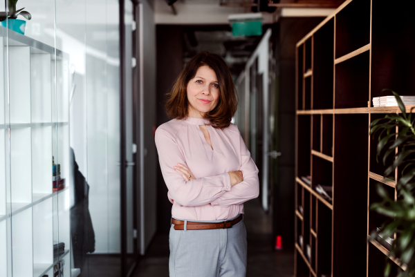 A portrait of businesswoman standing in an office building with crossed arms, looking at camera.