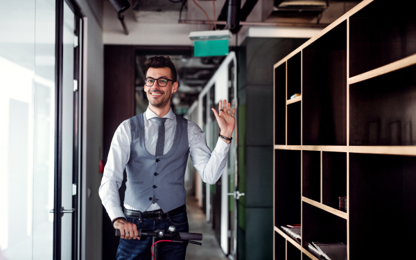 Young businessman with motor scooter in an office building, waving at somebody.