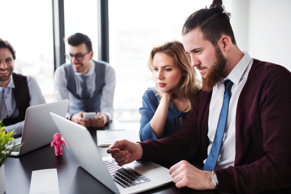 A group of young cheerful business people with laptop sitting in an office, talking.