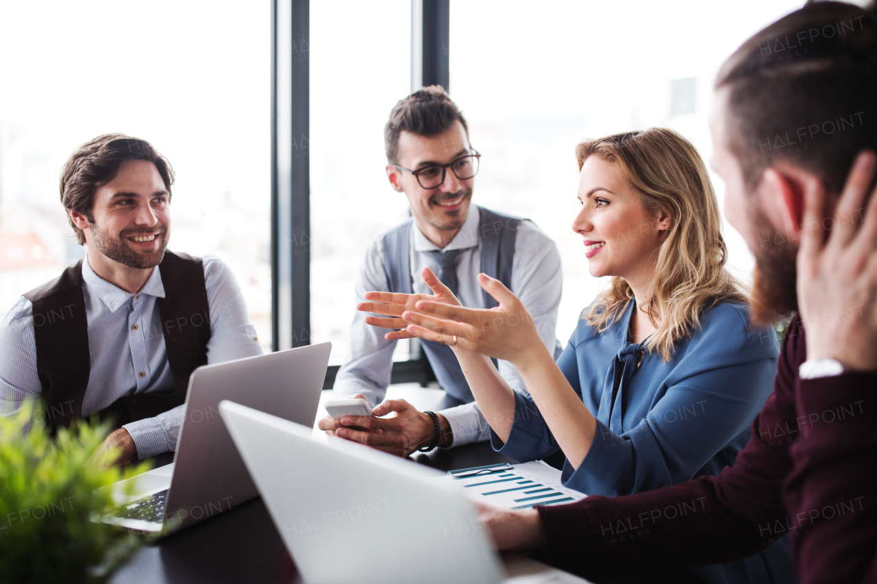 A group of young cheerful business people with laptop sitting in an office, talking.