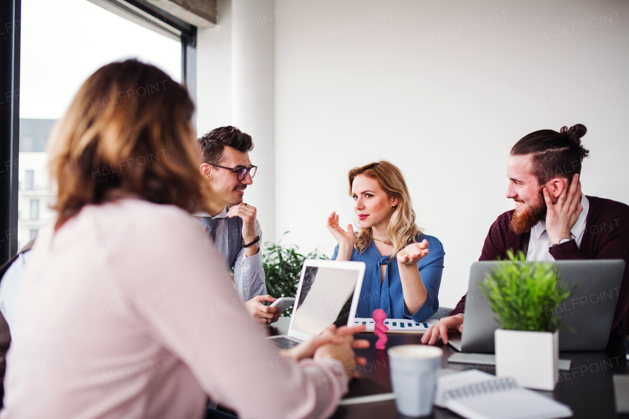 A group of young cheerful business people with laptop sitting in an office, talking.