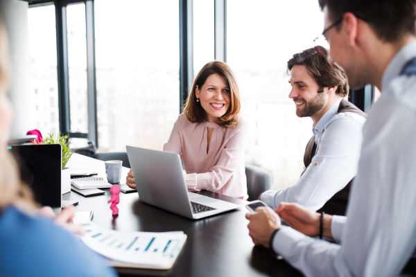 A group of young cheerful business people with laptop sitting in an office, talking.