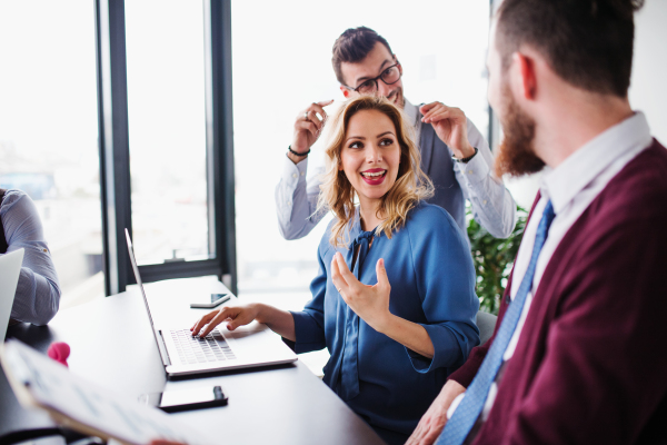 A group of young cheerful business people with laptop sitting in an office, talking.