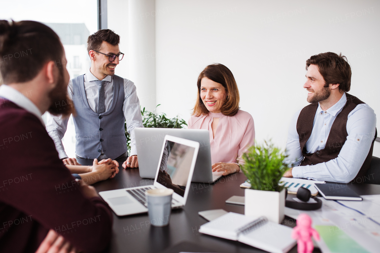 A group of young cheerful business people with laptop sitting in an office, talking.