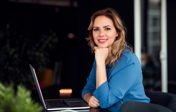 Young beautiful businesswoman with laptop sitting in an office, looking at camera.