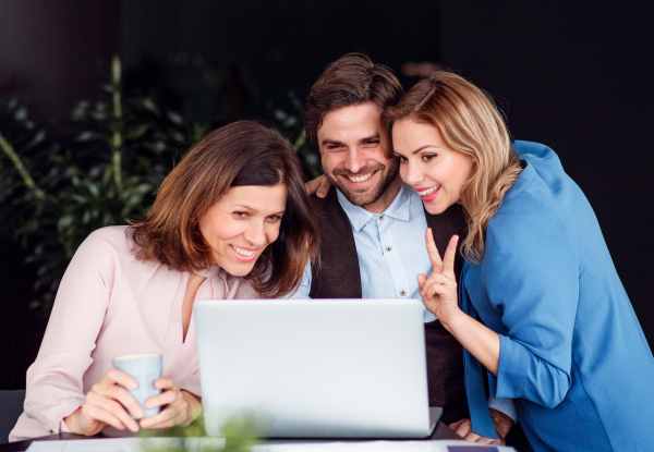 A group of cheerful business people sitting in an office, using laptop.